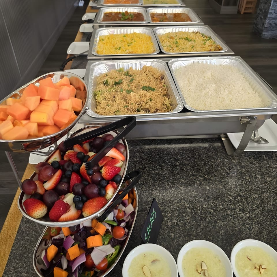 A buffet line with various Indian dishes, including rice, curries, fruit, and salads.