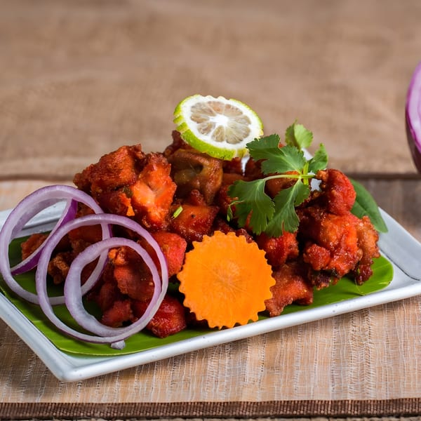 Charminar Indian Grill & Bar's Chicken 65, garnished with lemon, cilantro, red onion, and carrot.