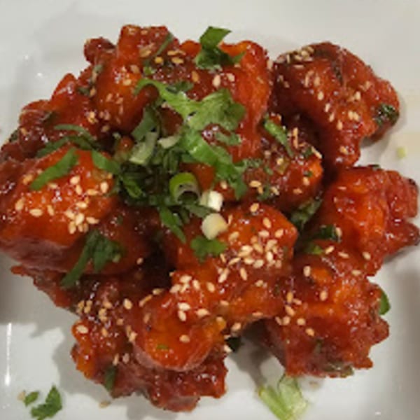 Charminar Indian Grill & Bar's Gobi Manchurian, a vibrant red dish topped with sesame seeds and green herbs.